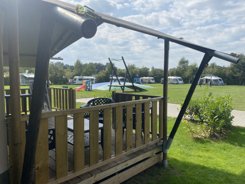 Blick von einem Safari-Zelt mit Veranda auf Campingplatz Dal van de Mosbeek, Niederlande, mit Wohnwagen und Spielplatz.