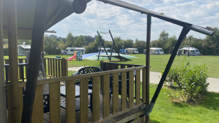 Blick von einem Safari-Zelt mit Veranda auf Campingplatz Dal van de Mosbeek, Niederlande, mit Wohnwagen und Spielplatz.