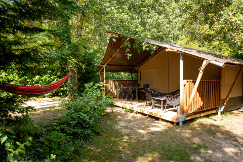 Safari-Zelt im Grünen mit Veranda, Sitzgelegenheiten und roter Hängematte links im Wald.