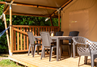 Outdoor seating area at a safari tent with plastic chairs and a table on a wooden deck under cover.