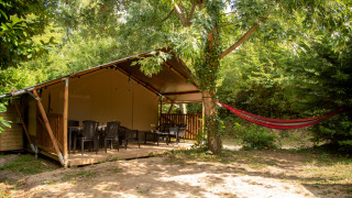 Tenda safari con bagno privato nel bosco, ampia veranda, sedie di plastica e amaca all’aperto.