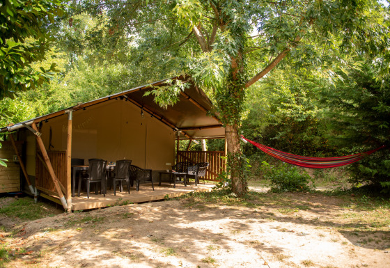 Safari tent with private bathroom in the woods, spacious deck, plastic chairs, and a hammock outside.