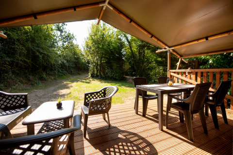 View from Safari tent with sanitary at Campsite Fargogne, outdoor deck with seating and dining tables.