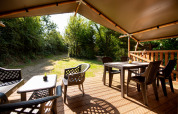 View from Safari tent with sanitary at Campsite Fargogne, outdoor deck with seating and dining tables.