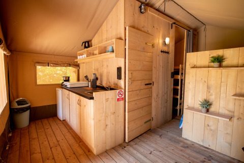 Interior of Safari tent with wooden kitchen and bathroom at Campsite Fargogne, France, featuring cozy design.