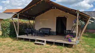 Safari telt med veranda, havemøbler og blomsterkrukker, placeret på en græsplæne under en skyet himmel.