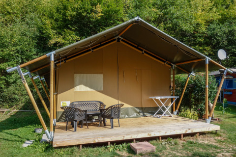 Safari-telt med overdækket terrasse, havemøbler og egen sanitetsfacilitet nær grøn skov.