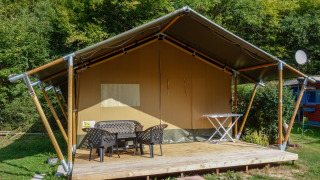 Safari tent with covered terrace, outdoor furniture, and private sanitary facilities by the woods.