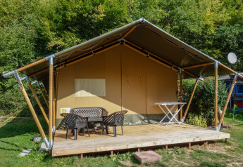 Safari tent with covered terrace, outdoor furniture, and private sanitary facilities by the woods.