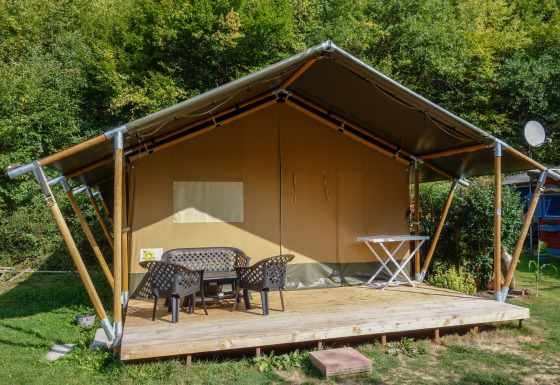 Tenda safari con veranda coperta, mobili da esterno e servizi igienici privati vicino al bosco.