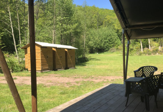 View from wooden porch toward sanitary cabins and greenery at Safari tent, Campsite Bockenauer Schweiz, Germany.