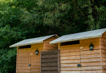 Two small wooden sanitary cabins with lamps next to each other, surrounded by forest at Campsite Bockenauer Schweiz.
