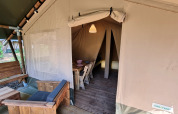 Ingang van een safaritent met houten meubels, eethoek en gezellige kampeeromgeving.