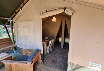 Ingang van een safaritent met houten meubels, eethoek en gezellige kampeeromgeving.