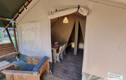 Eingang zu einem Safarizelt mit Holzmöbeln, Essbereich und gemütlicher Atmosphäre auf dem Campingplatz.