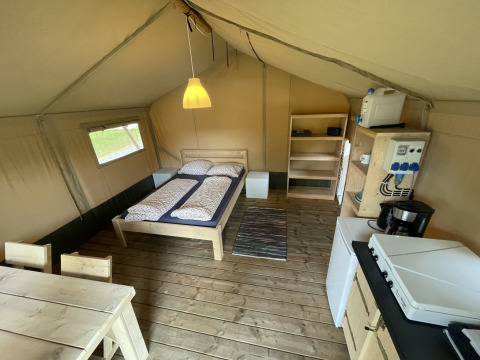 Binnenkant van een safaritent op Camping du Rivage in Luxemburg met bed, keuken en eetruimte.