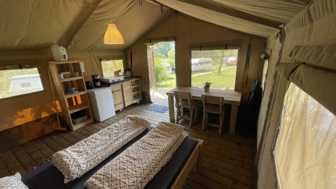 Binnenzicht van een safaritent op Camping du Rivage in Luxemburg met bedden, keuken en eettafel.