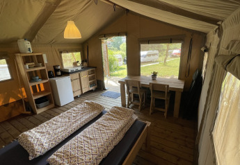 Vue intérieure d'une tente safari au Camping du Rivage au Luxembourg, avec lits, cuisine et table à manger.