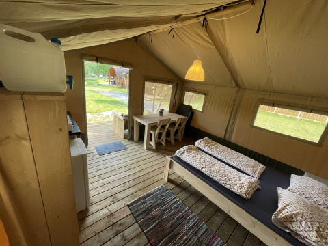 Binnen in een safaritent op Camping du Rivage, Luxemburg, met houten meubilair en zicht op het groen.