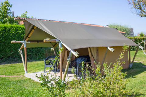 Safari tent Duo Lodge with shaded terrace and plastic patio chairs, set on grassy lawn during summer.