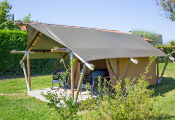 Safari tent Duo Lodge with shaded terrace and plastic patio chairs, set on grassy lawn during summer.