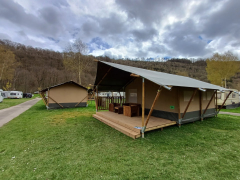 Tienda safari en el camping la Roche en Bélgica, con terraza de madera y colinas pintorescas de fondo.