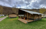 Tienda safari en el camping la Roche en Bélgica, con terraza de madera y colinas pintorescas de fondo.