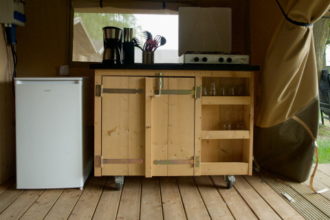 Innenbereich einer Safarizeltküche mit Minikühlschrank, Holzschrank und Gasherd auf Campingplatz la Roche.