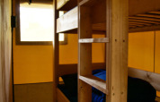 Vista interior de una tienda safari con una litera de madera, ropa de cama azul y ventana iluminada.