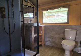 Baño en tienda safari con ducha, inodoro y ventana en Camping Vallee de L'Our, Luxemburgo.
