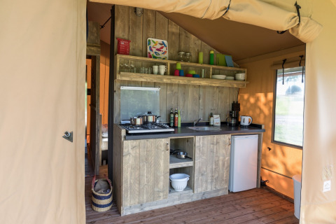 Angolo cottura in una tenda safari con armadi in legno, fornello, lavello, frigo ed utensili sugli scaffali.