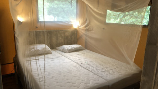 Lit avec moustiquaire dans une tente safari, fenêtres sur la nature, ambiance chaleureuse et lumineuse.