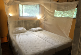 Lit avec moustiquaire dans une tente safari, fenêtres sur la nature, ambiance chaleureuse et lumineuse.