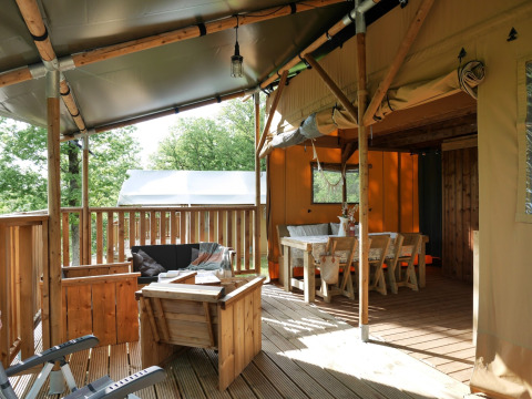 Safari telt med overdækket terrasse, træmøbler og spiseplads, omgivet af grønne træer i naturen.
