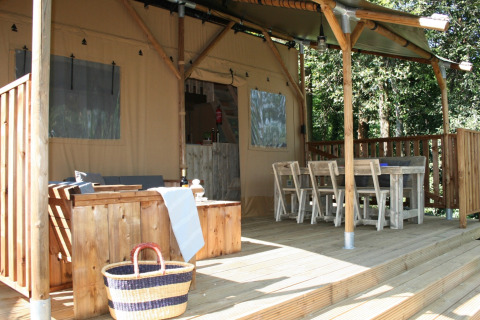 Safari tent met houten terras, buitensalon, eettafel en stoelen, midden in een bosrijke omgeving.