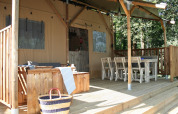 Terrasse en bois d'une tente safari, mobilier extérieur, table à manger et panier dans un cadre boisé.