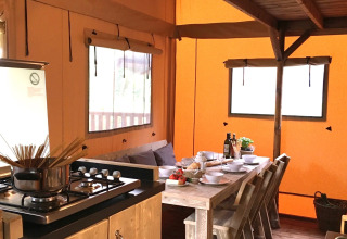 Binnenzicht van een safaritent met houten keuken, gedekte tafel en knusse zitbank met kussens.