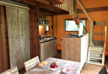 Interieur van een safaritent met houten meubilair, eetgedeelte, keuken en trap naar de vide.
