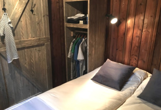 Interior de una tienda Lodge con paredes de madera, cama y armario abierto en el camping l’Ardéchois, Francia.