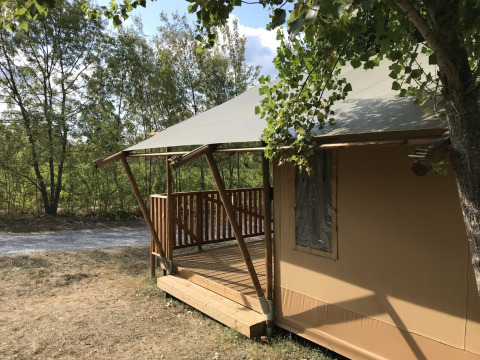 Safari tent at Campsite Saint Amand in France with a wooden deck and surrounded by lush green trees.