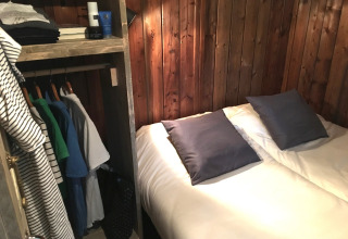 Binnenzijde van een lodge tent met sanitair: tweepersoonsbed, houten wand en een open kleerkast.