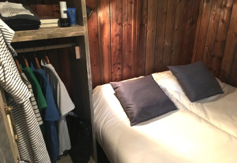 Binnenkant van een lodge tent met sanitair: tweepersoonsbed, houten wanden en een open kast.