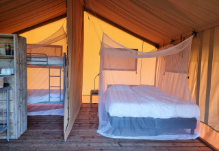 Innenansicht eines Safarizeltes mit Doppelbett und Etagenbett, beide mit Moskitonetzen auf Holzboden.