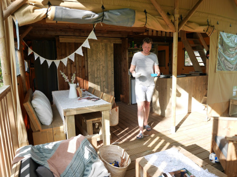 Man standing on the veranda of a Lodge tent safari tent at Campsite Paradiso in Italy, sunny and cozy.