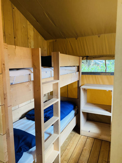 Houten stapelbedden en rekken in een safaritent op Camping De Rammelbeek in Nederland.