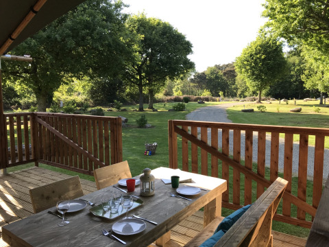 Veranda in legno di una tenda safari al Campeggio de Kerleyou in Francia con vista sul prato verde.