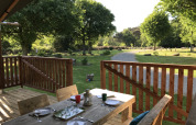 Wooden deck at a safari tent at Campsite de Kerleyou in France overlooking a green lawn and trees.