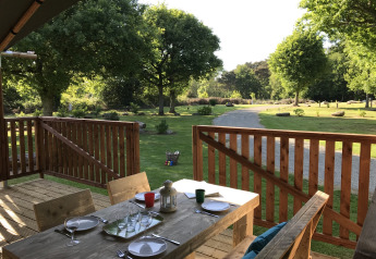 Træterrasse ved en safaritelt på Campingplads de Kerleyou i Frankrig med udsigt til en grøn have.