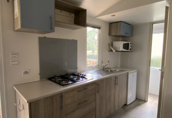 Compacte keuken in een mobiel huisje op Camping Le Céou in Frankrijk, met gasvuur, wasbak en microgolf.