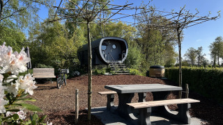 Außenansicht des Anthropod Tiny House mit Picknicktisch, Bank, Fahrrad und Bäumen im Grünen.